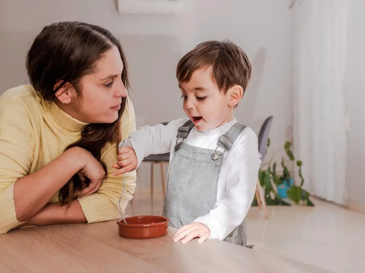 Mama patrzy z czułością na swojego synka, który jak małe **dziecko introwertyk** z zaciekawieniem bada zawartość miseczki.