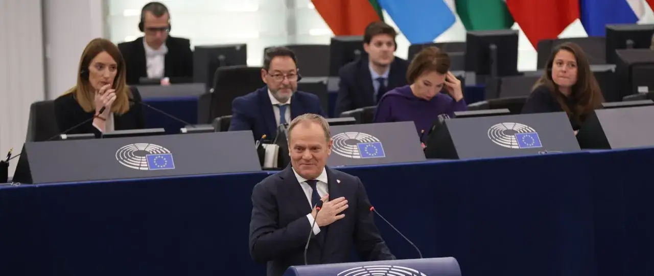 Donald Tusk, z ręką na sercu, przemawia w Parlamencie Europejskim. Jego działania dla Polski są tematem dyskusji.
