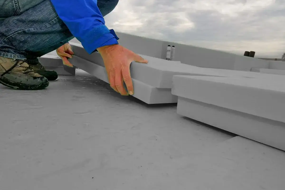 Ręce układają warstwy szarego styroduru na płaskiej powierzchni. To pokazuje, czym kleić styrodur, by stworzyć izolację.