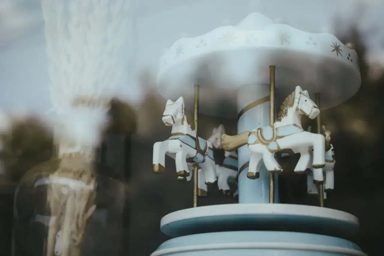 Urocze gadżety z koniem: miniaturowa karuzela z białymi konikami i złotymi detalami, ozdobiona gwiazdkami.