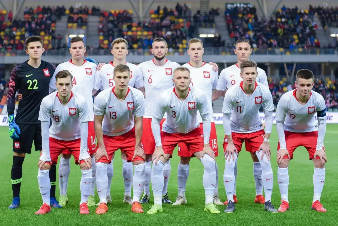 Drużyna Polski w białych strojach, z numerami na koszulkach. W pierwszym rzędzie piłkarze z numerami 18, 13, 3, 15, 19. W drugim rzędzie bramkarz z numerem 22, a obok niego piłkarze z numerami 4, 5, 6, 0, 11.