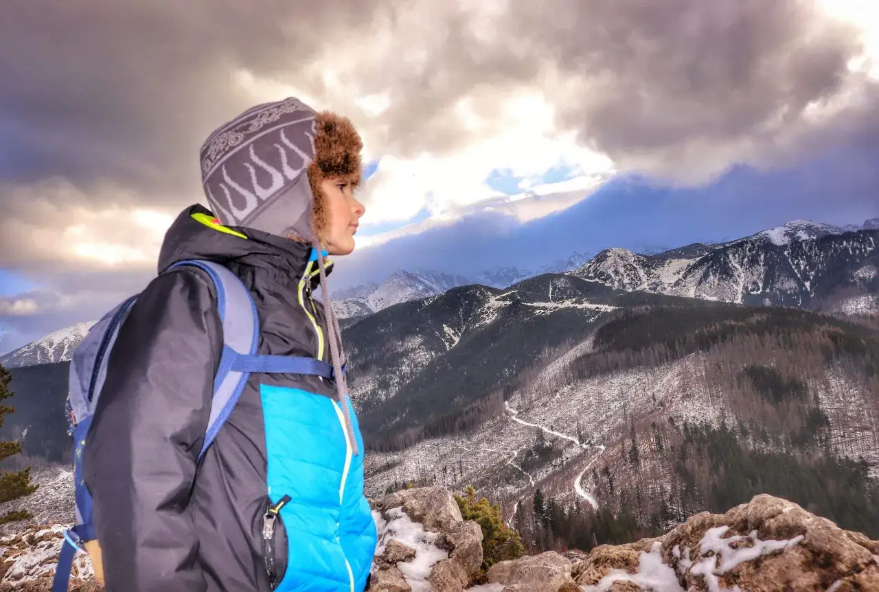 Chłopiec w czapce z uszami patrzy na malowniczy szlak na Nosal. Góry pokryte śniegiem i chmury tworzą dramatyczny krajobraz.