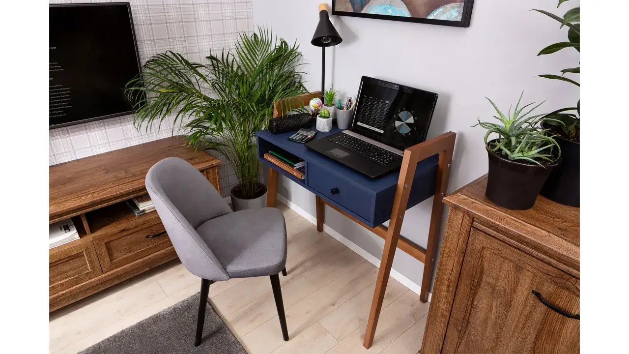 Przytulny gabinet w domu: granatowe biurko z laptopem, rośliny i wygodne krzesło.