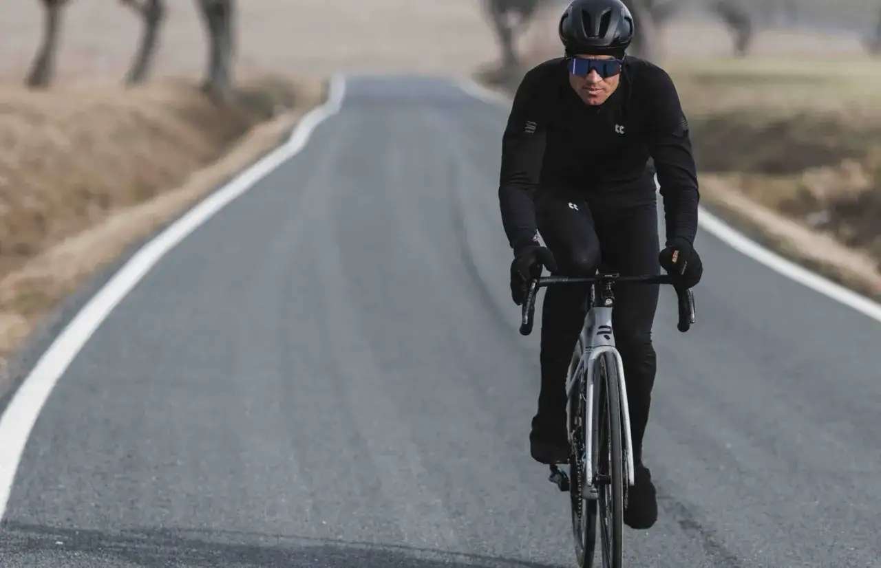 Kolarz w czarnym stroju, kasku i okularach na drodze. Idealny przykład, jak się ubrać na rower 15 stopni.