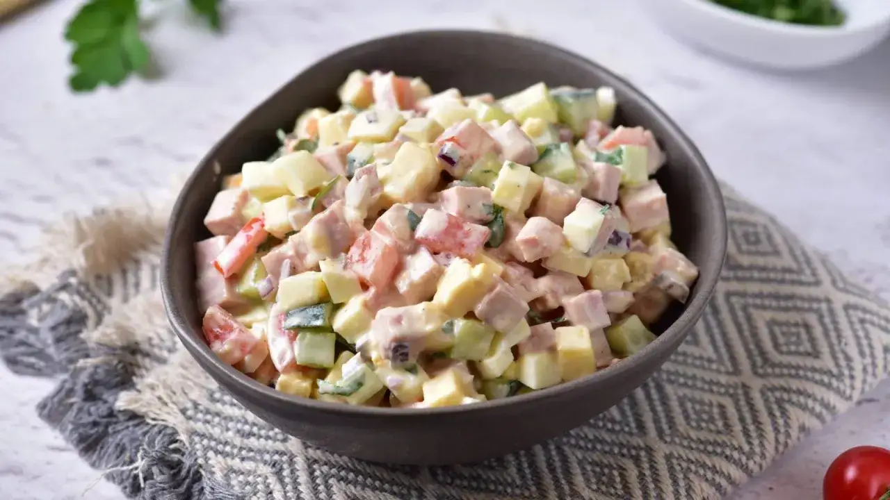 Pyszna sałatka z szynką i ż&oacute;łtym serem i jajkiem, z dodatkiem og&oacute;rka i pomidora, polana kremowym sosem.