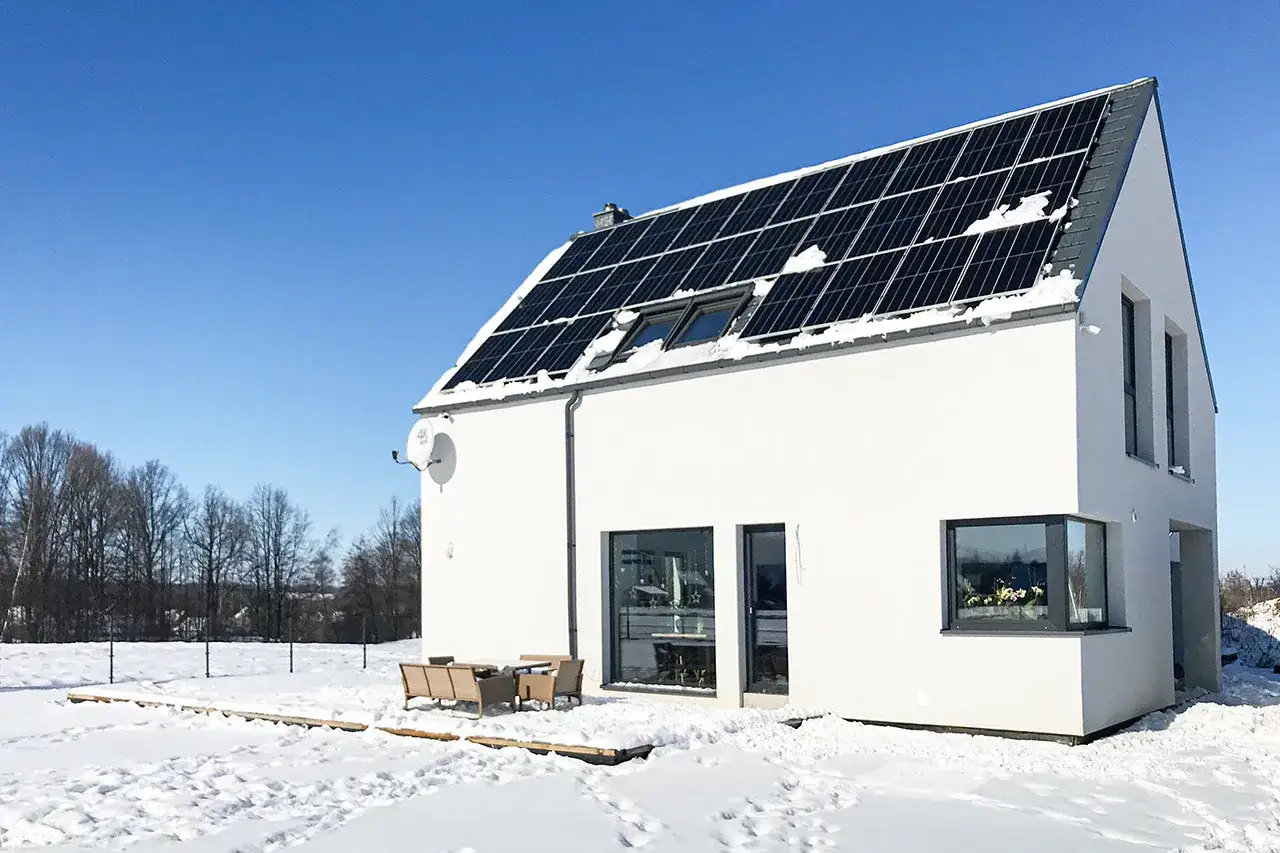 Nowoczesny dom z panelem fotowoltaicznym na dachu, otoczony śniegiem. Projekt instalacji fotowoltaicznej w zimowej scenerii.