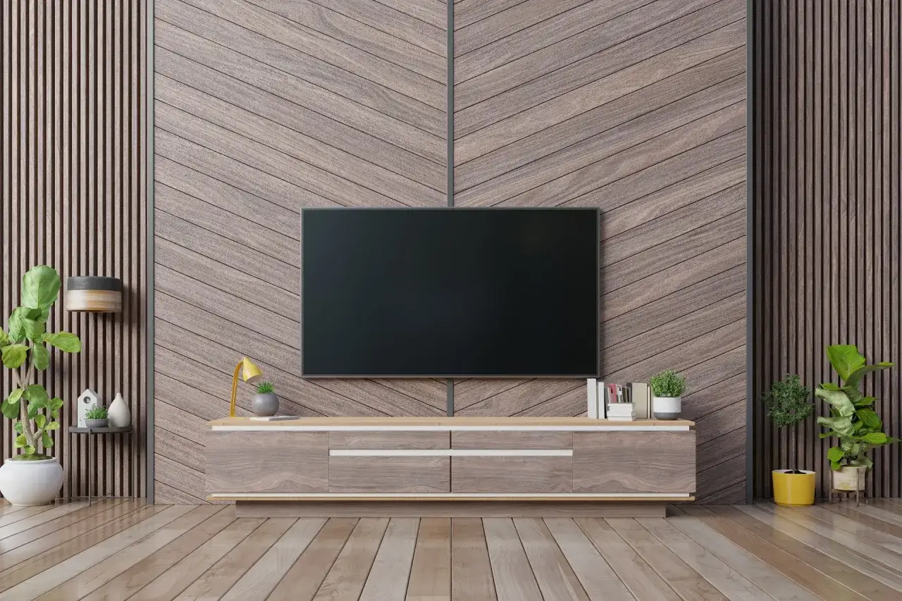 Nowoczesny salon z telewizorem na ścianie w jodełkę. Drewniane panele tworzą eleganckie tło dla mebli i roślin.