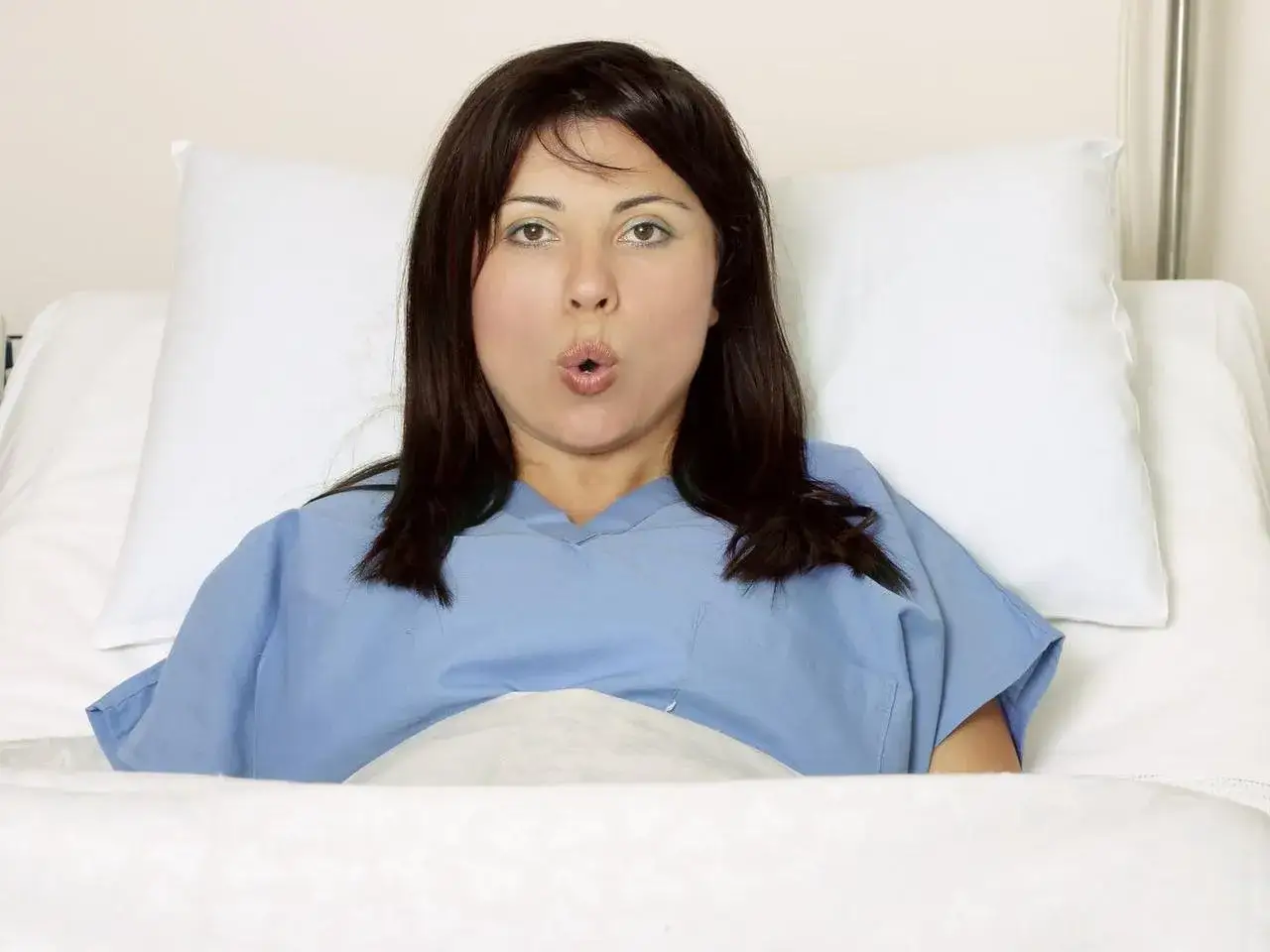 Kobieta w niebieskiej koszuli szpitalnej, z wyrazem zaskoczenia na twarzy, leży w ł&oacute;żku. Czeka na kolejne skurcze co godzinę.