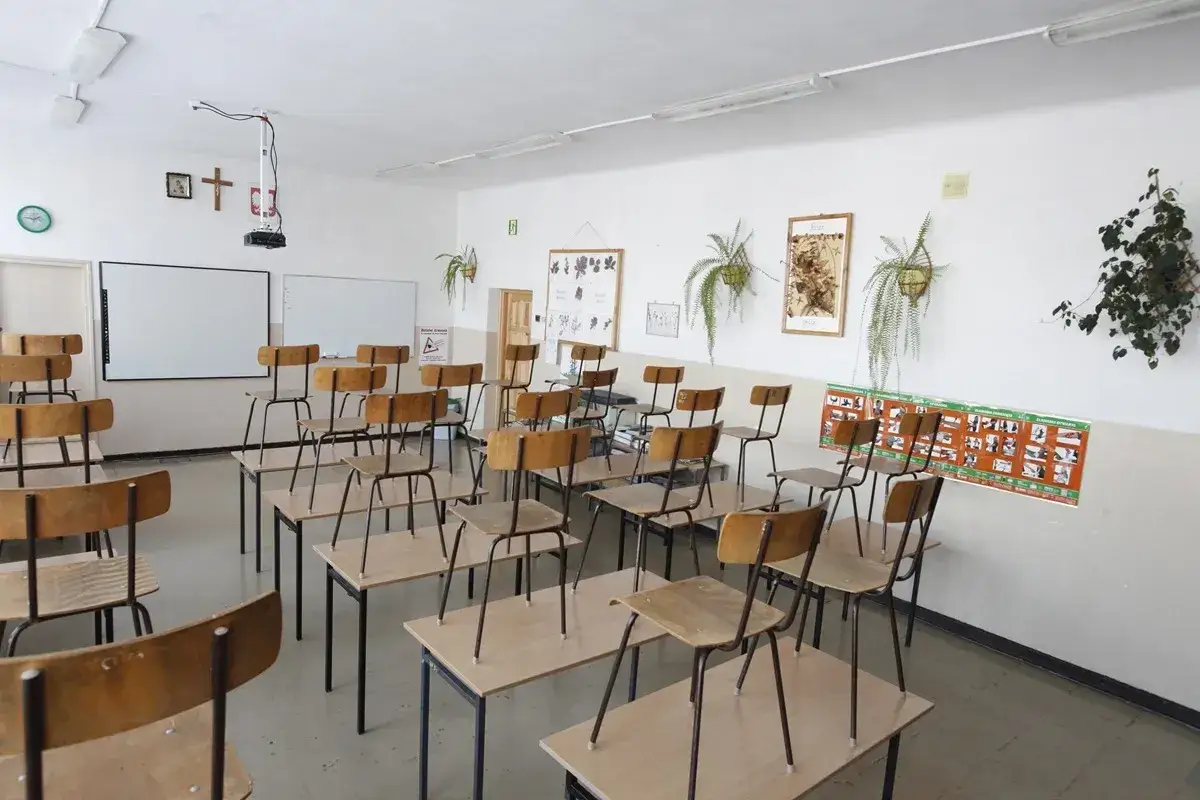 Puste krzesła i ławki w sali lekcyjnej, kiedy nauczyciel nie może przeprowadzić lekcji. Na ścianach wiszą tablice i rośliny.