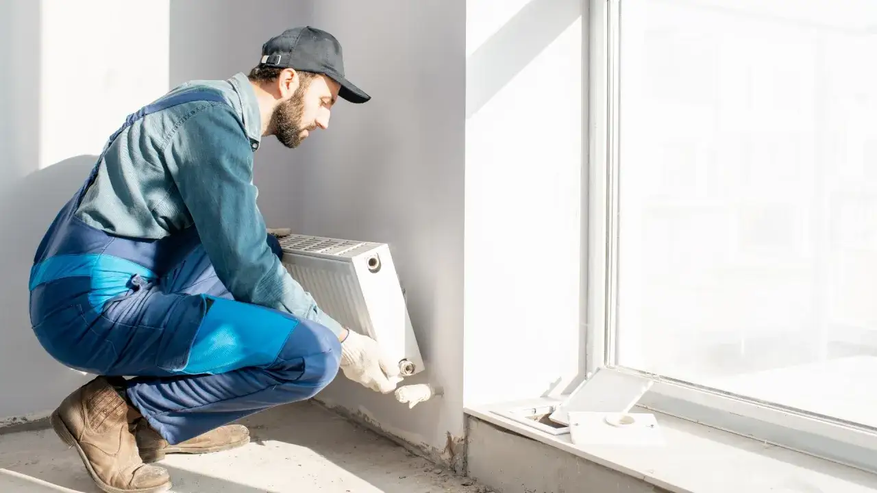 Instalator w kombinezonie montuje grzejnik, korzystając z dofinansowania do wymiany grzejników.