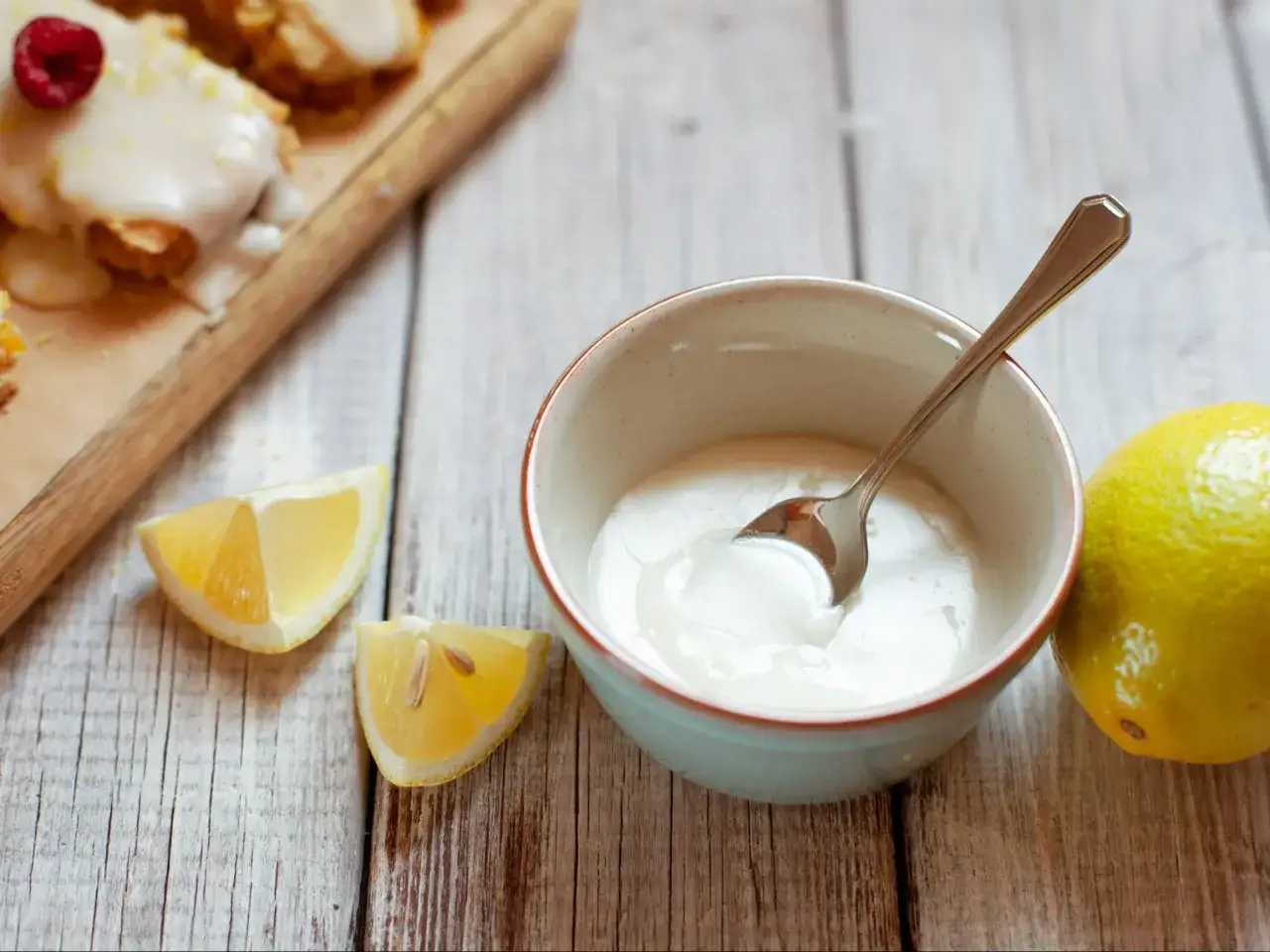 Jak zrobić lukier ze zwykłego cukru? Miseczka z lukrem, cytryny i gotowe ciastka na desce.