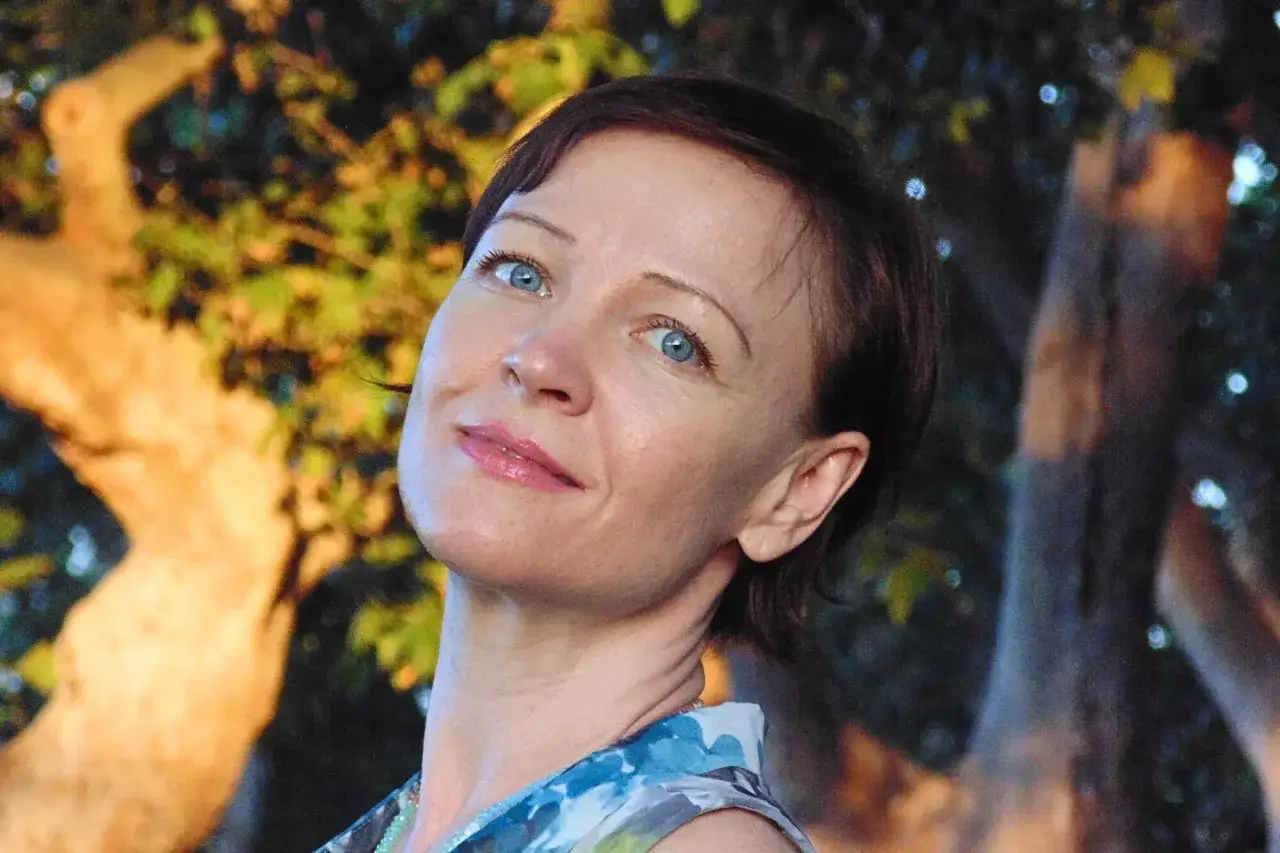 Kobieta z błękitnymi oczami, w letniej sukience, wpatruje się w dal. Chce być sama, ciesząc się chwilą spokoju wśr&oacute;d natury.