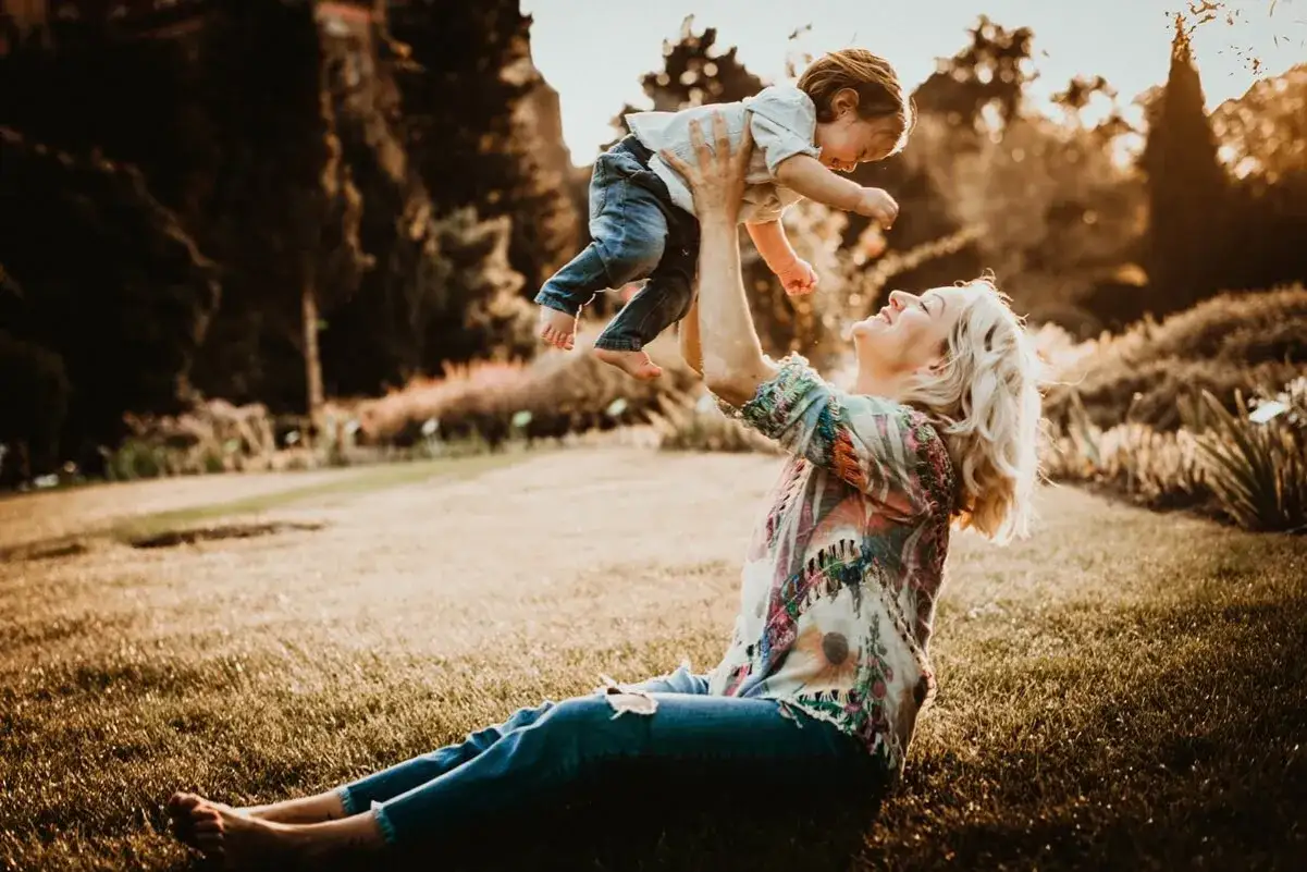Piękna mama podrzuca dziecko w złotym świetle. Wspaniałe pomysły na sesje zdjęciowe dzieci w plenerze.