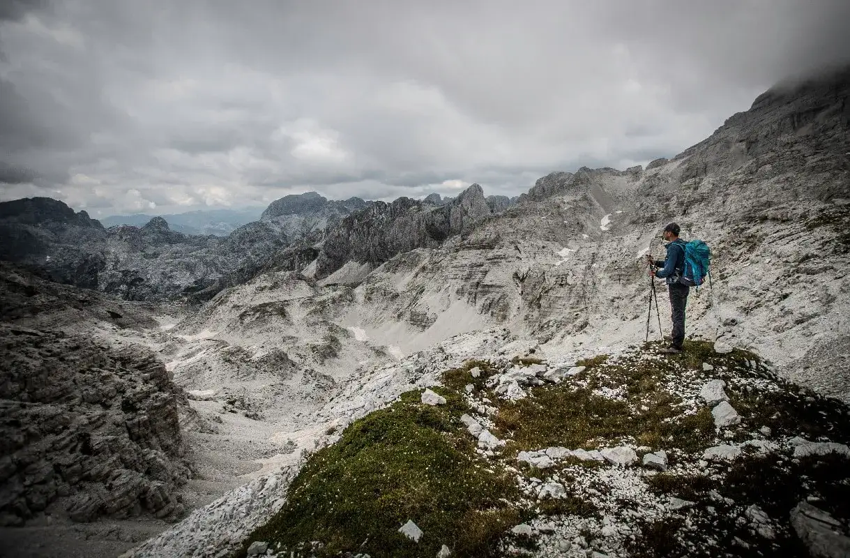 Samotny turysta z plecakiem i kijkami stoi na skraju urwiska, podziwiając surowe piękno przeklętych g&oacute;r.