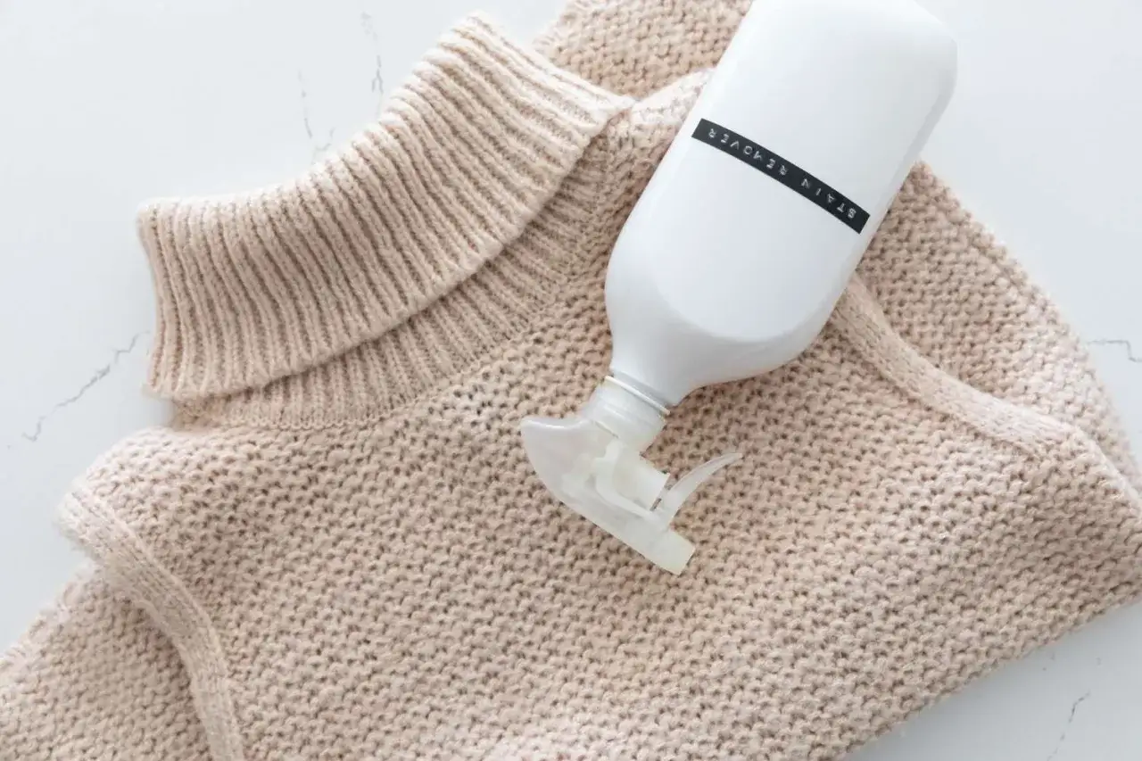 Beżowy sweter z akrylu i butelka ze środkiem do usuwania plam.