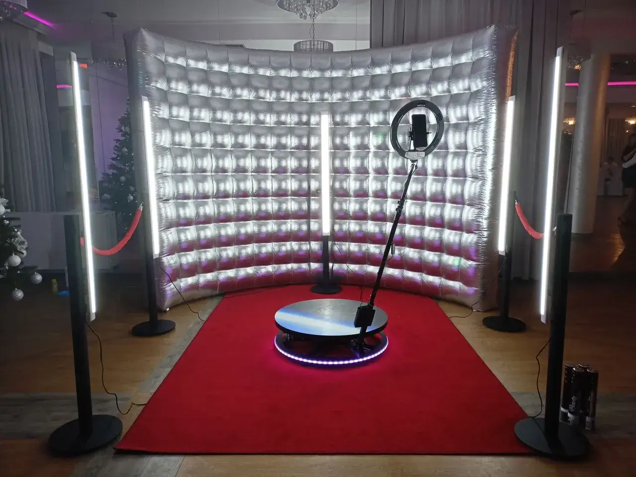 Zastanawiasz się, ile kosztuje fotobudka na imprezę? Oto nowoczesna, srebrna fotobudka z obrotową platformą, czerwonym dywanem i oświetleniem, gotowa na Twoje wydarzenie.