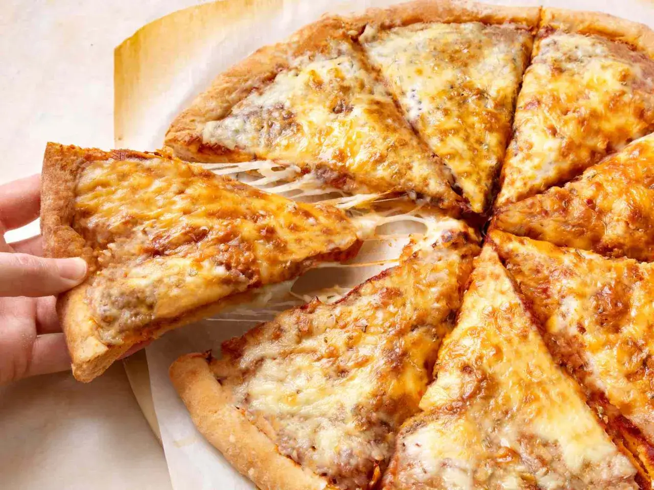 Ręka podnosi kawałek pizzy z ciągnącym się serem. Widać, ile piec pizzy zostało pokrojone.