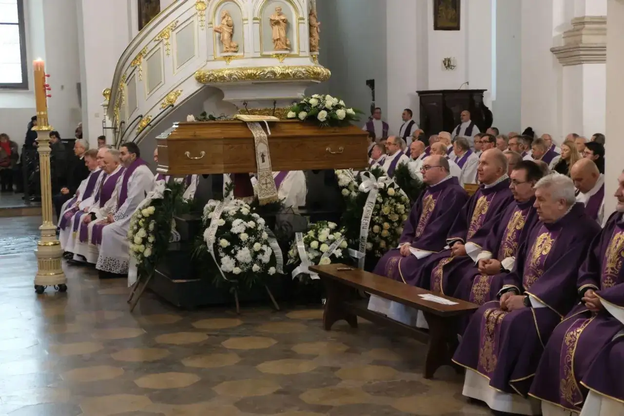 Uroczystość pogrzebowa z trumną i wieńcami. Duchowni w purpurowych szatach siedzą w ławkach. Ile trwa różaniec na pogrzebie? Zwykle około 20-30 minut.