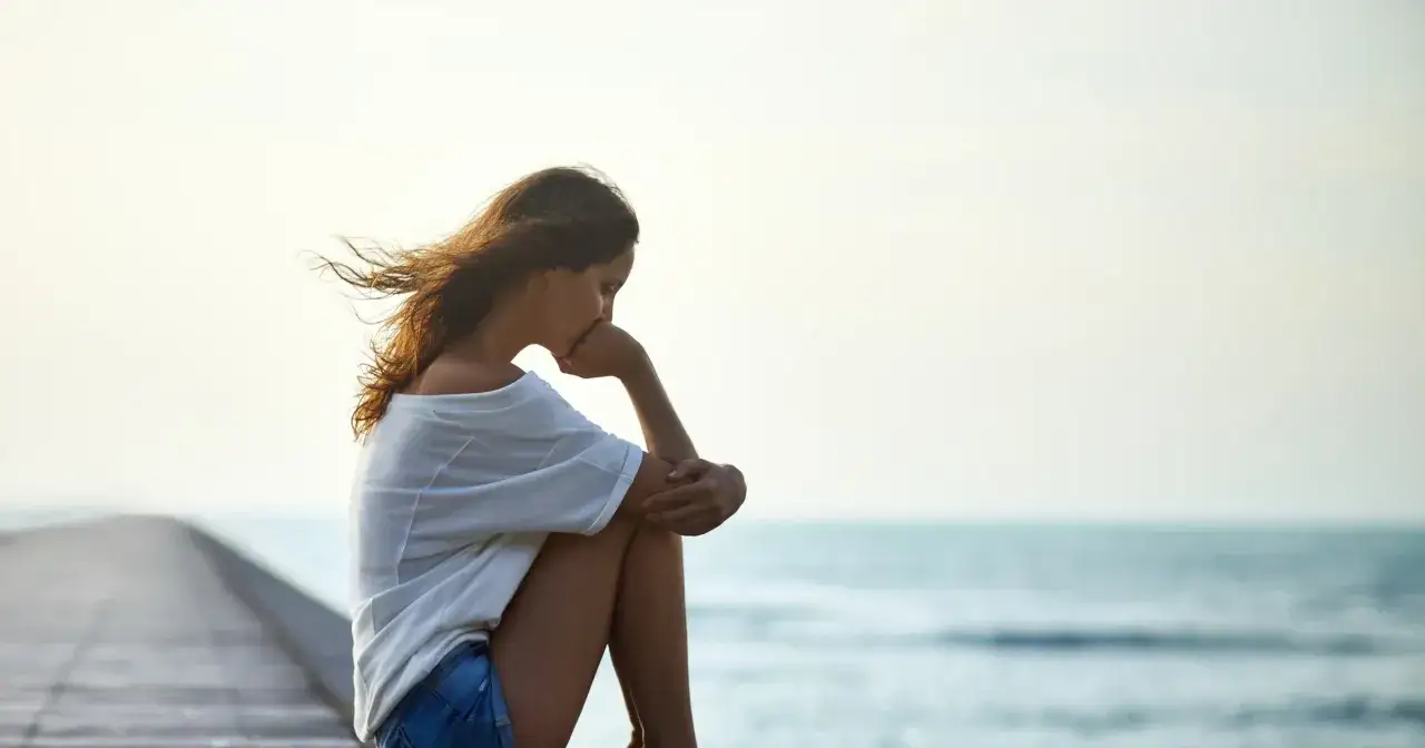 Siedząca na pomoście dziewczyna zamyślona, wiatr rozwiewa jej włosy. W jej postawie widać tęsknotę za kimś.