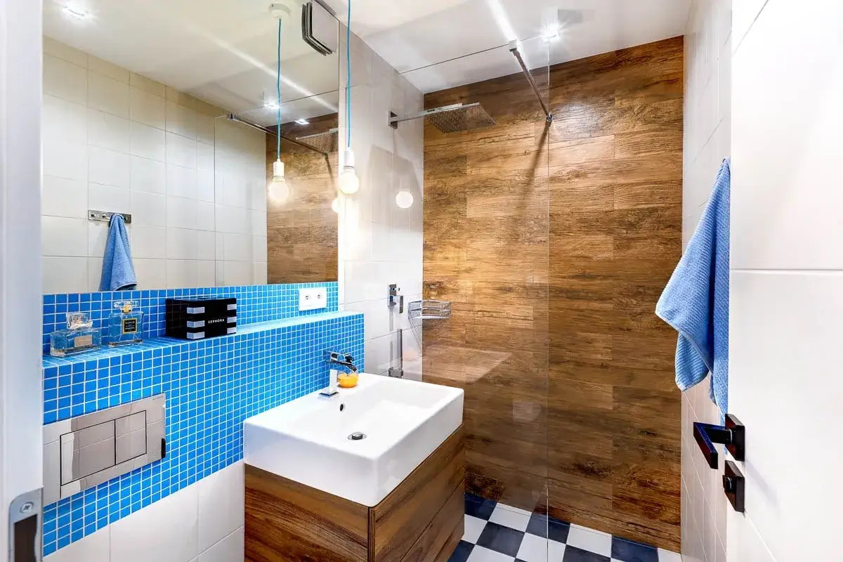 Nowoczesna łazienka z niebieskimi mozaikami i drewnianą ścianą w prysznicu. Inspiracja, jak wykafelkować małą łazienkę.