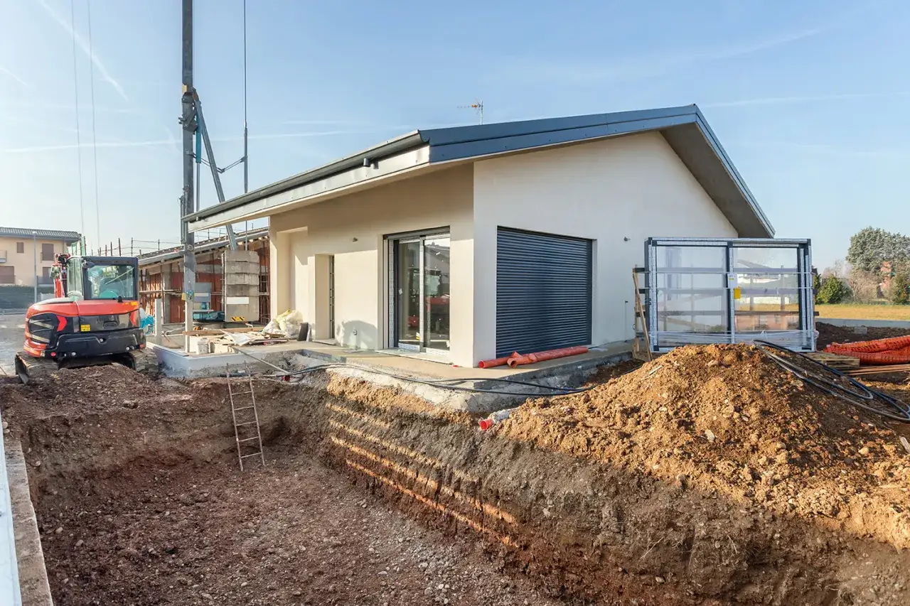 Budowa domu 70m2: wykop pod fundamenty, koparka i częściowo wykończony budynek.