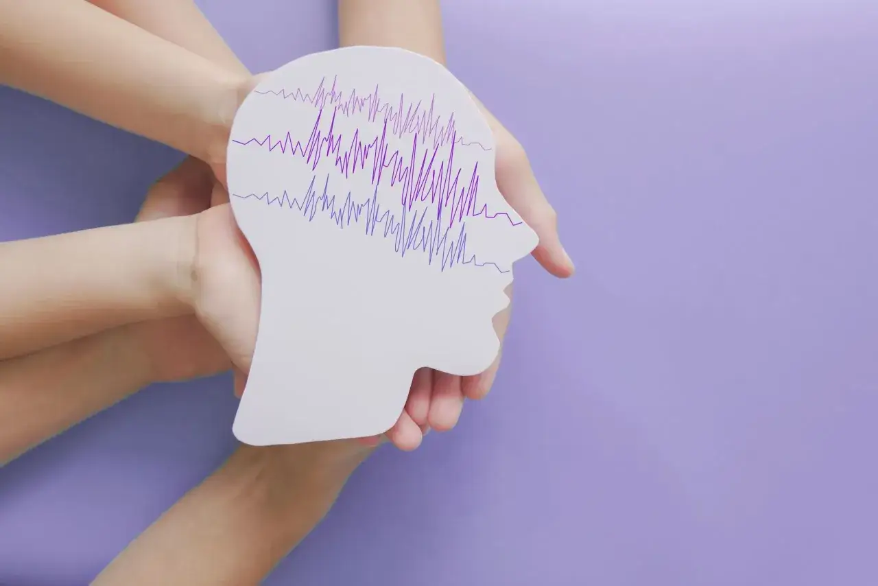 Dłonie trzymają biały profil głowy z fioletowymi, nieregularnymi liniami symbolizującymi nietypowe objawy padaczki.
