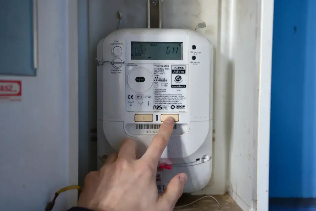 Dłoń naciska przycisk licznika energii elektrycznej. Czy licznik energii elektrycznej może oszukiwać? To pytanie nurtuje wielu konsumentów.