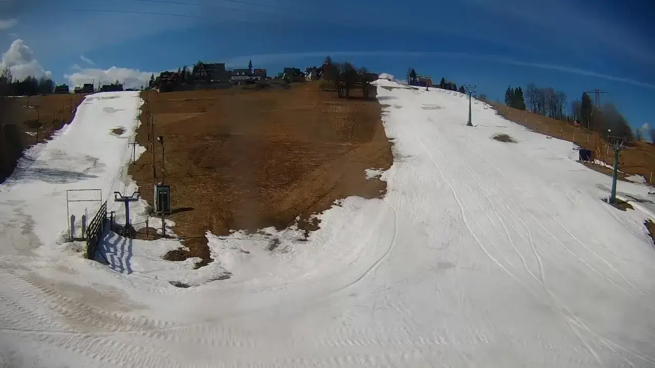 Widok z kamery na stok w Bukowinie Tatrzańskiej. Widać wyciąg krzesełkowy, ślady po nartach i budynki w tle.