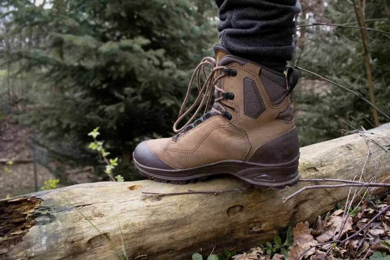 Brązowe buty trekkingowe na powalonym pniu. Nowe buty trekkingowe obcierają pięty, co utrudnia wędr&oacute;wkę po lesie.