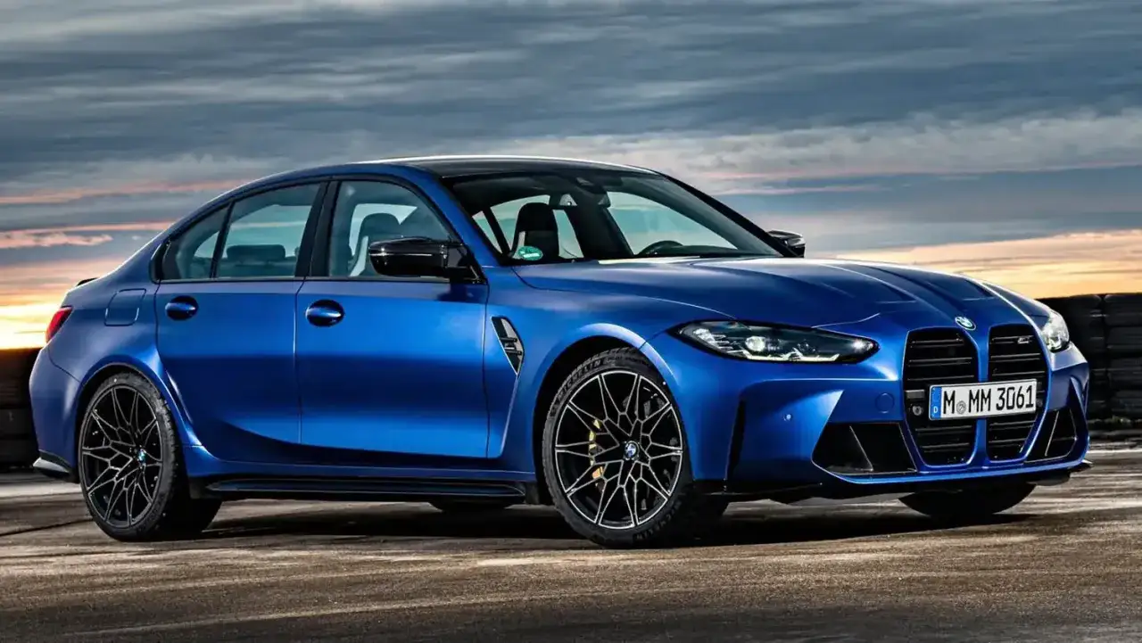 Niebieskie BMW M3 G80 z czarnymi felgami i przyciemnianymi szybami, gotowe do jazdy po zachodzie słońca.