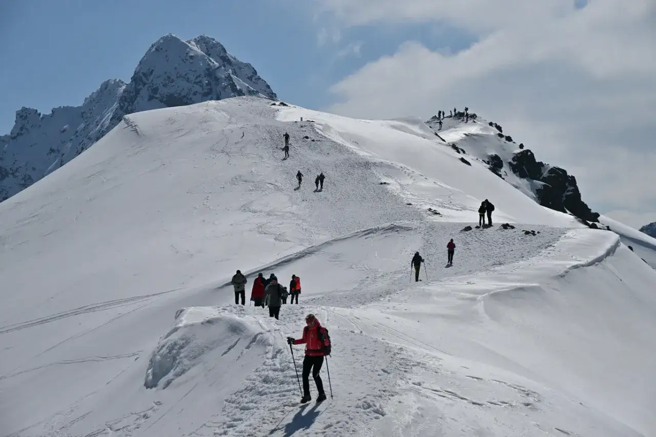 Grupa turyst&oacute;w na ośnieżonym szlaku, zbliżająca się do szczytu. Widok na wejście na Kasprowy Wierch w słoneczny dzień.