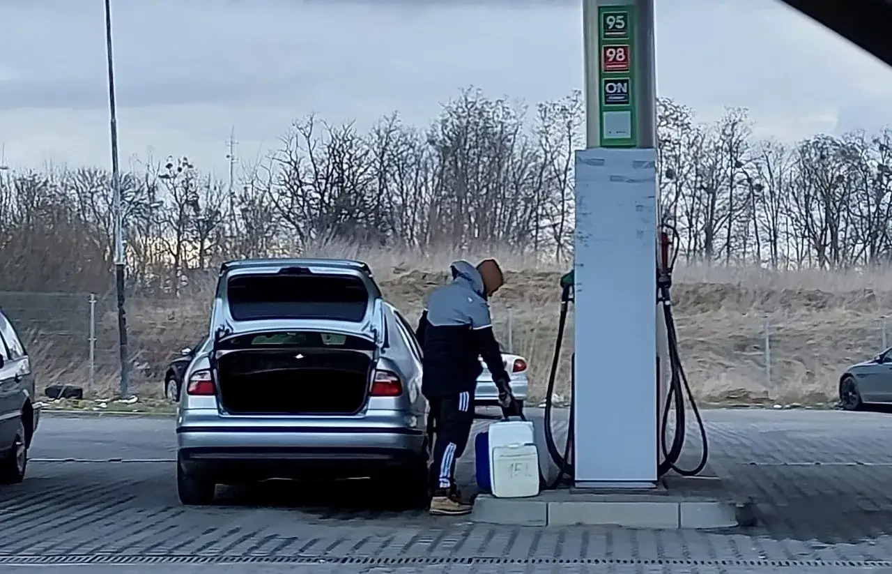 Mężczyzna tankuje paliwo do kanistra, przygotowując się do podróży. Zastanawia się, ile paliwa można przewieźć przez granicę.