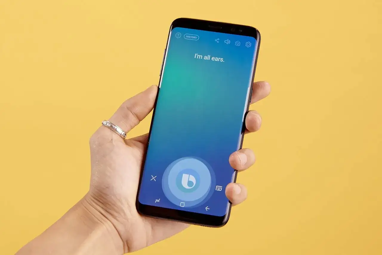 Dłoń trzyma smartfon z włączonym asystentem Bixby po polsku. Na ekranie widnieje napis 