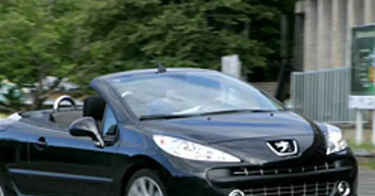 Czarny kabriolet Peugeot 207 CC z opuszczonym dachem jedzie po drodze.