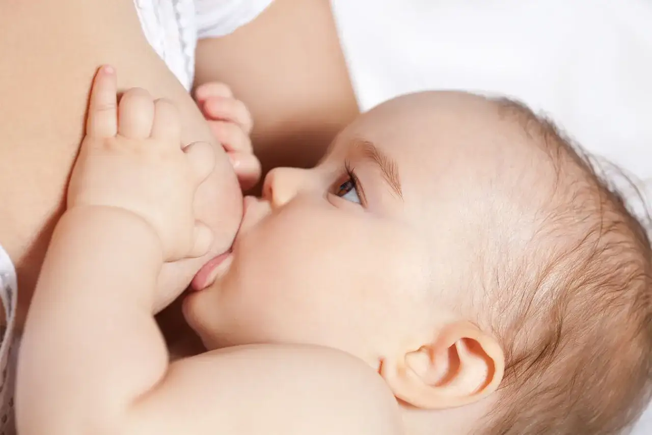 Malutkie rączki pomagają w karmieniu, a mama zastanawia się, jak pobudzić laktację. Dziecko ssie pierś, czując się bezpiecznie i kochane.