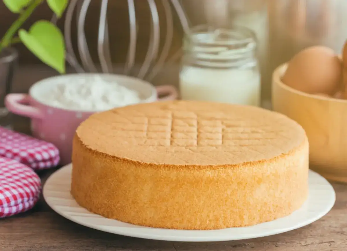 Idealny biszkopt bezglutenowy przepis. Puszysty, złocisty, gotowy do dekoracji. W tle składniki: mąka, mleko, jajka.