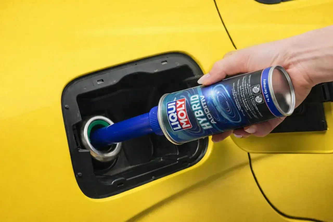 Ręka wlewa dodatek do benzyny Liqui Moly Hybrid Additiv do baku żółtego samochodu.