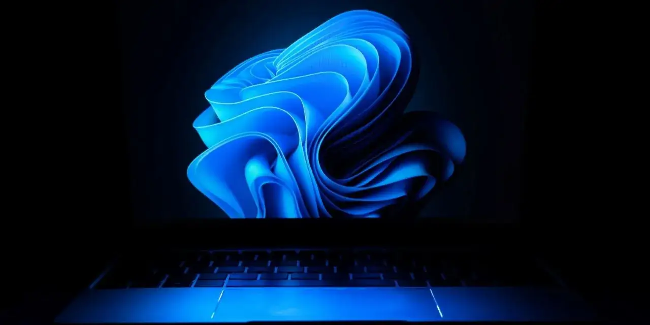 Niebieski, falujący wygaszacz ekranu Windows 11 na ciemnym tle, nad podświetlaną klawiaturą laptopa.