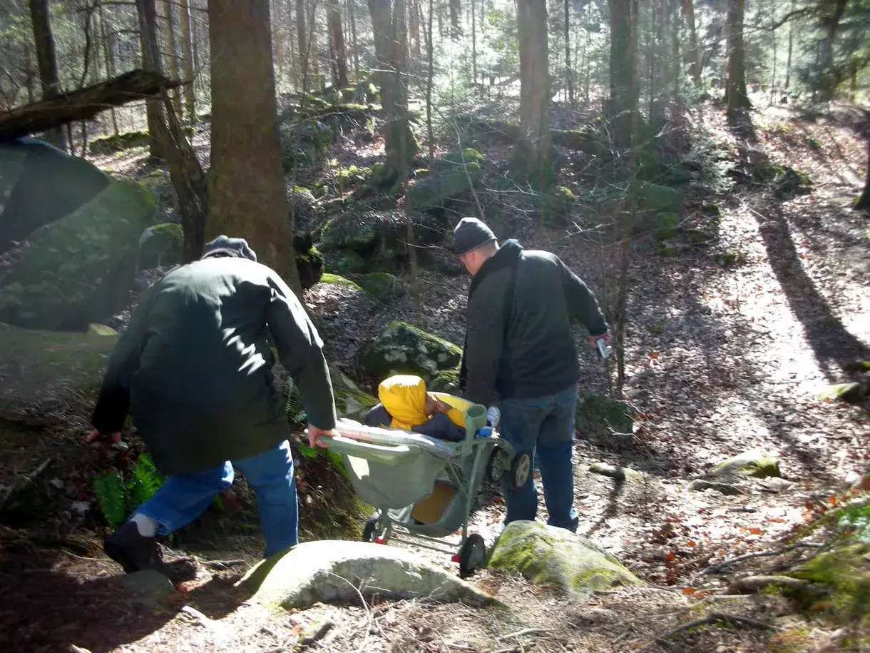 Dw&oacute;ch mężczyzn pcha w&oacute;zek z dzieckiem po leśnym szlaku. Idealne miejsce na rodzinne wycieczki, gdy zastanawiasz się, jakie szlaki z dzieckiem w Zakopanem wybrać.