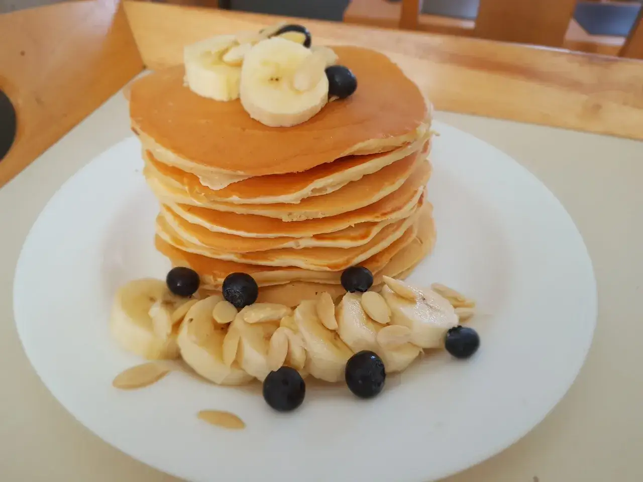 Stos puszystych pancakes, udekorowany plasterkami banana, jagodami i migdałami. Idealny pomysł, jak zrobić pancake na śniadanie.