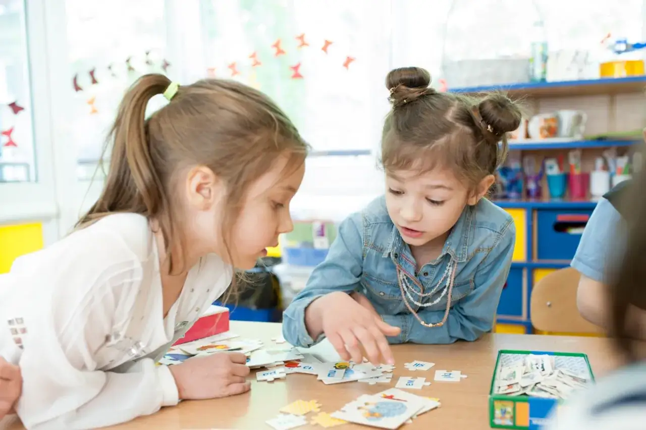 Dwie dziewczynki układają puzzle z literami, rozwiązując zadania dla 10 latka.