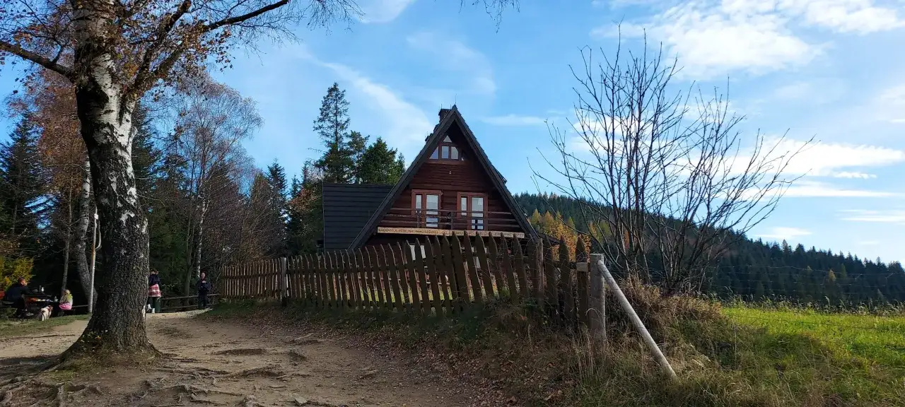 Drewniana bac&oacute;wka na Maciejowej z bali, otoczona płotem, w jesiennym krajobrazie Beskid&oacute;w.