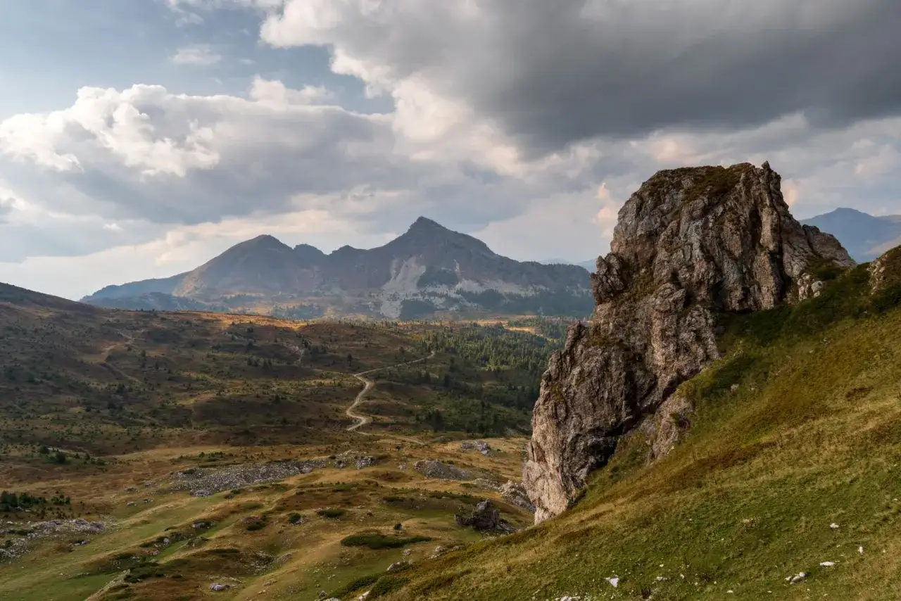 Majestatyczne góry na Półwyspie Bałkańskim, z krętą drogą wijącą się przez pagórkowaty krajobraz i skalistą formacją na pierwszym planie.