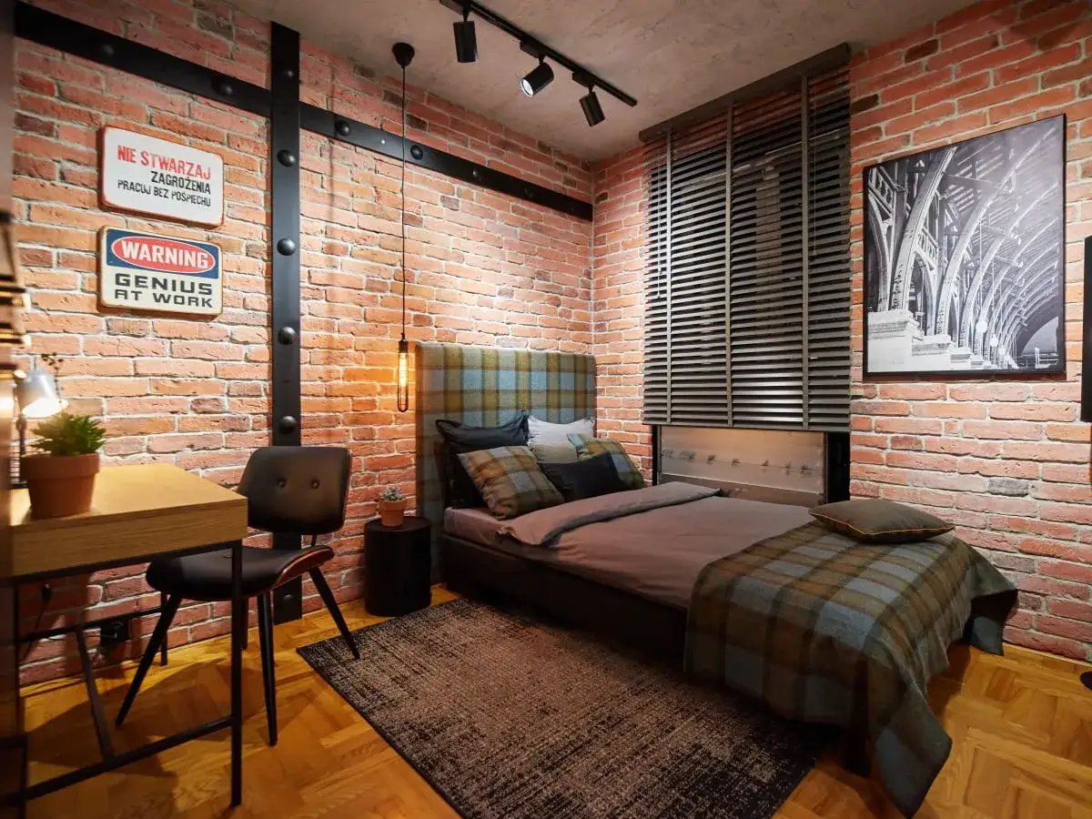 Męski pok&oacute;j inspiracje: loftowy styl z ceglaną ścianą, ł&oacute;żkiem w kratę i biurkiem.