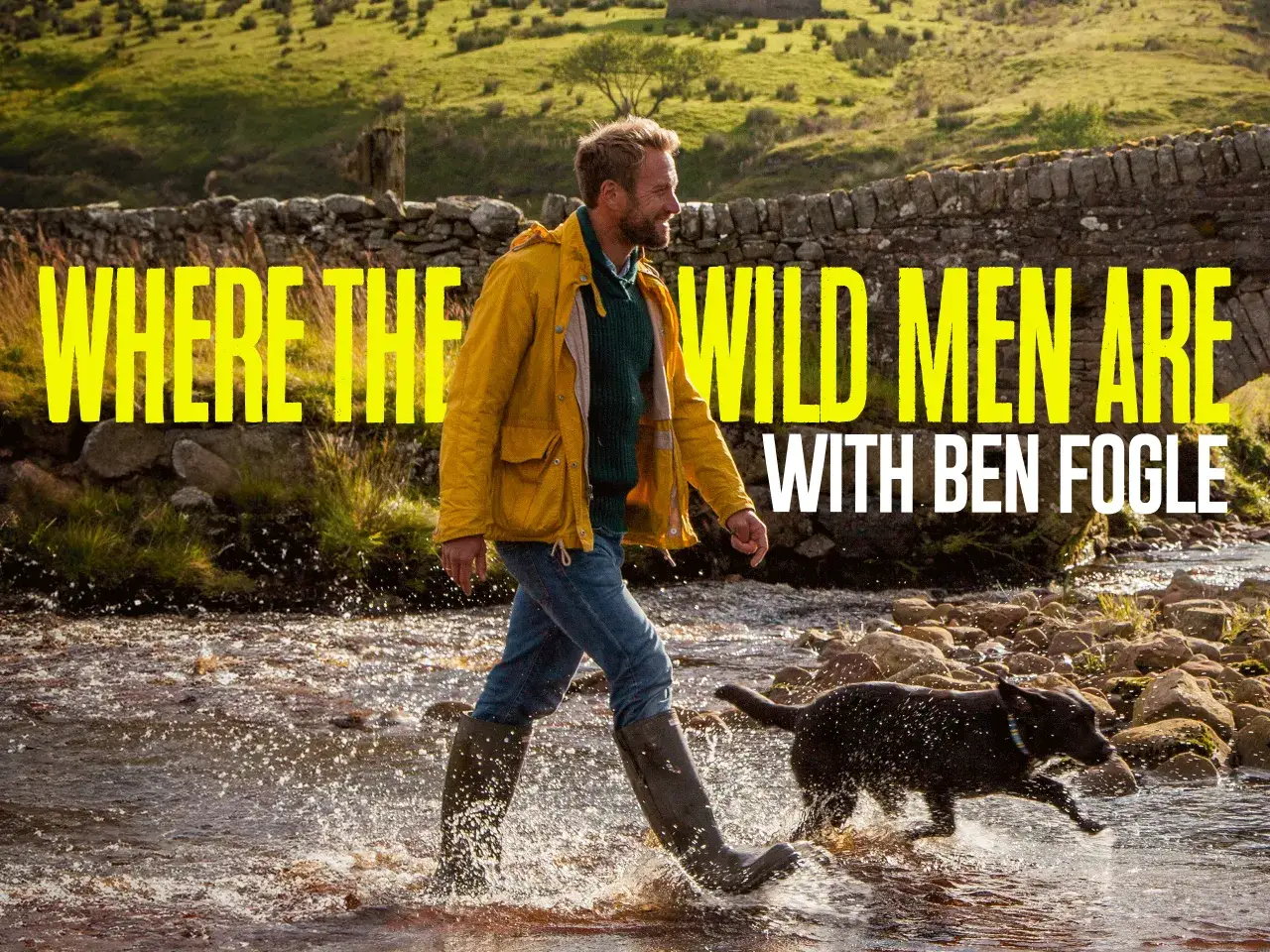 Ben Fogle w żółtej kurtce i pies przemierzają strumień. Witamy na odludziu, gdzie dzikie życie i przygoda czekają.