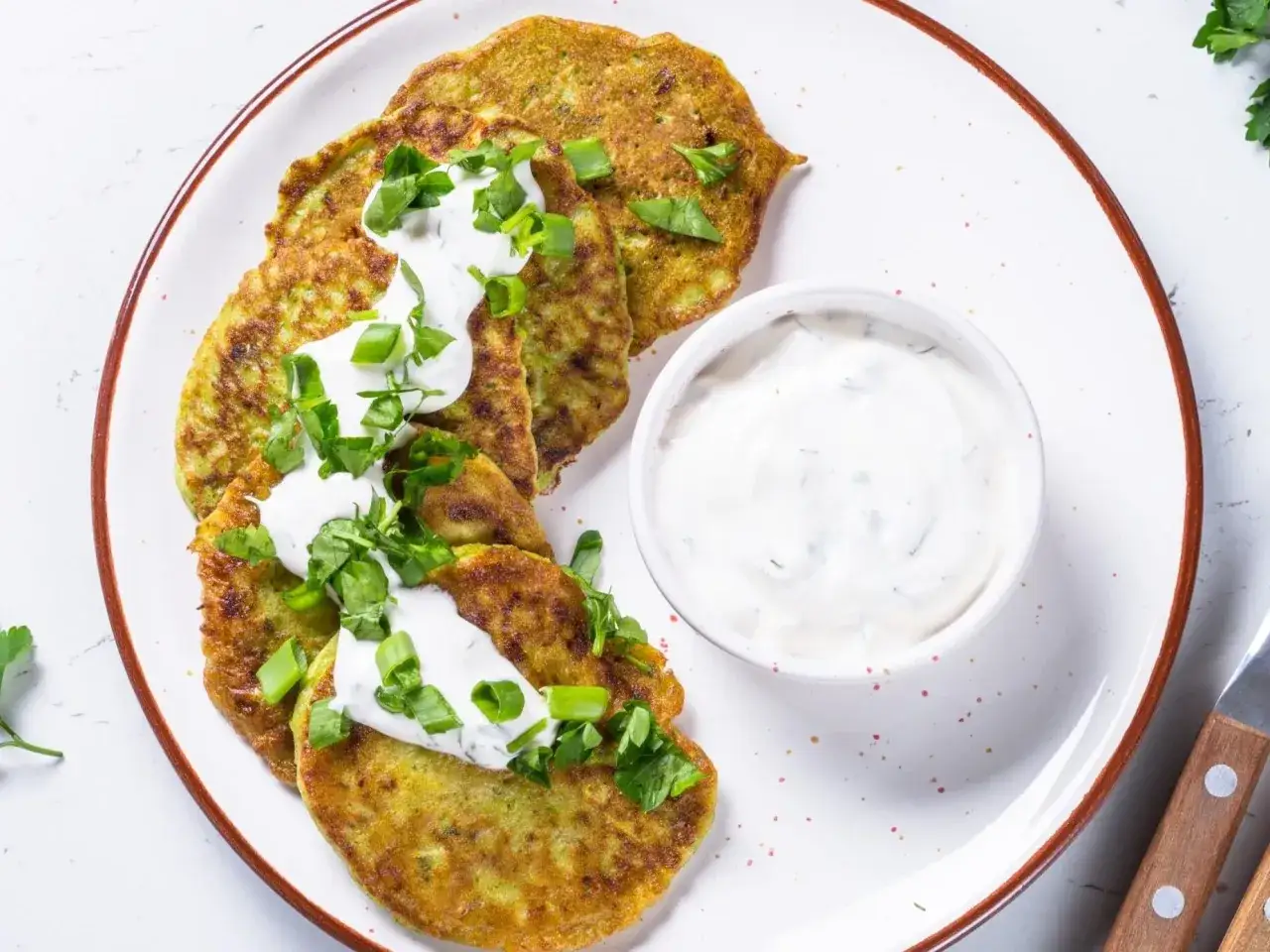 Placki z cukinii z jogurtowym dipem, posypane szczypiorkiem i natką. Idealne na lekki posiłek.