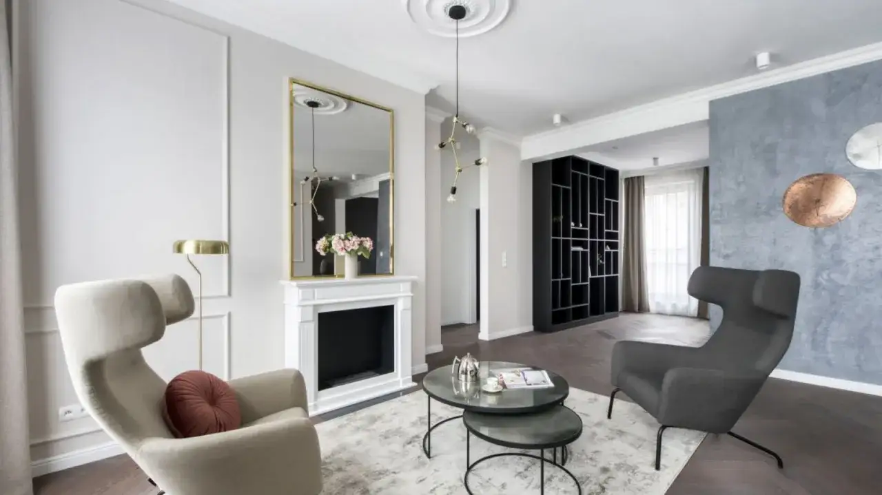 Eleganckie lustra na ścianie aranżacje w salonie z kominkiem, dwoma fotelami i regałem.