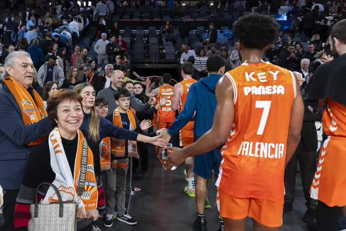 Jugadores de baloncesto del Valencia celebran tras un partido de la Europa League. Aficionados sonríen y saludan a los deportistas.