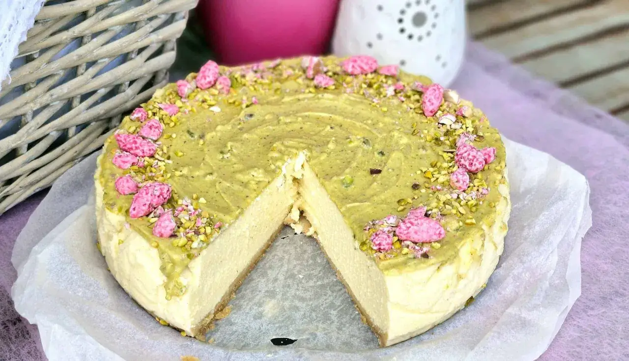 Idealny sernik, który nie opada, udekorowany pistacjami i różowymi cukierkami.