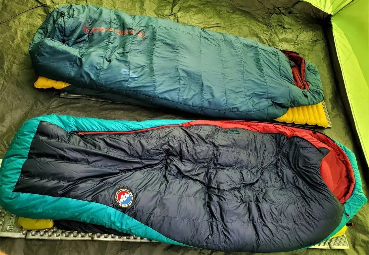 Dwa śpiwory, jeden zielony, drugi granatowo-turkusowy, leżą obok siebie. Kt&oacute;ry śpiw&oacute;r puchowy czy syntetyczny wybierzesz na noc?